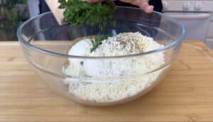 Mixing fresh herbs into a bowl of ricotta and mozzarella cheese on a wooden cutting board.